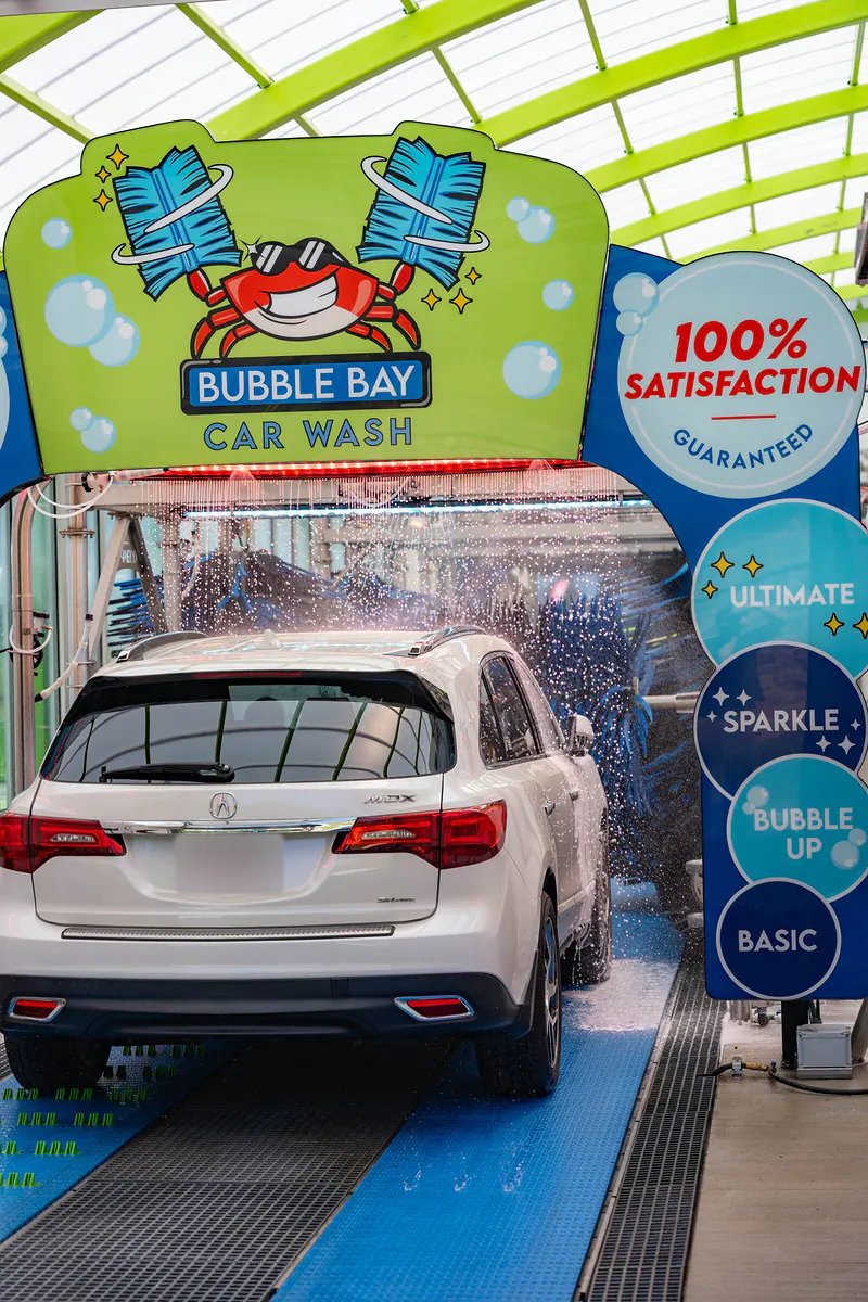 A white SUV rolling into the wash tunnel under the Bubble Bay crab arch